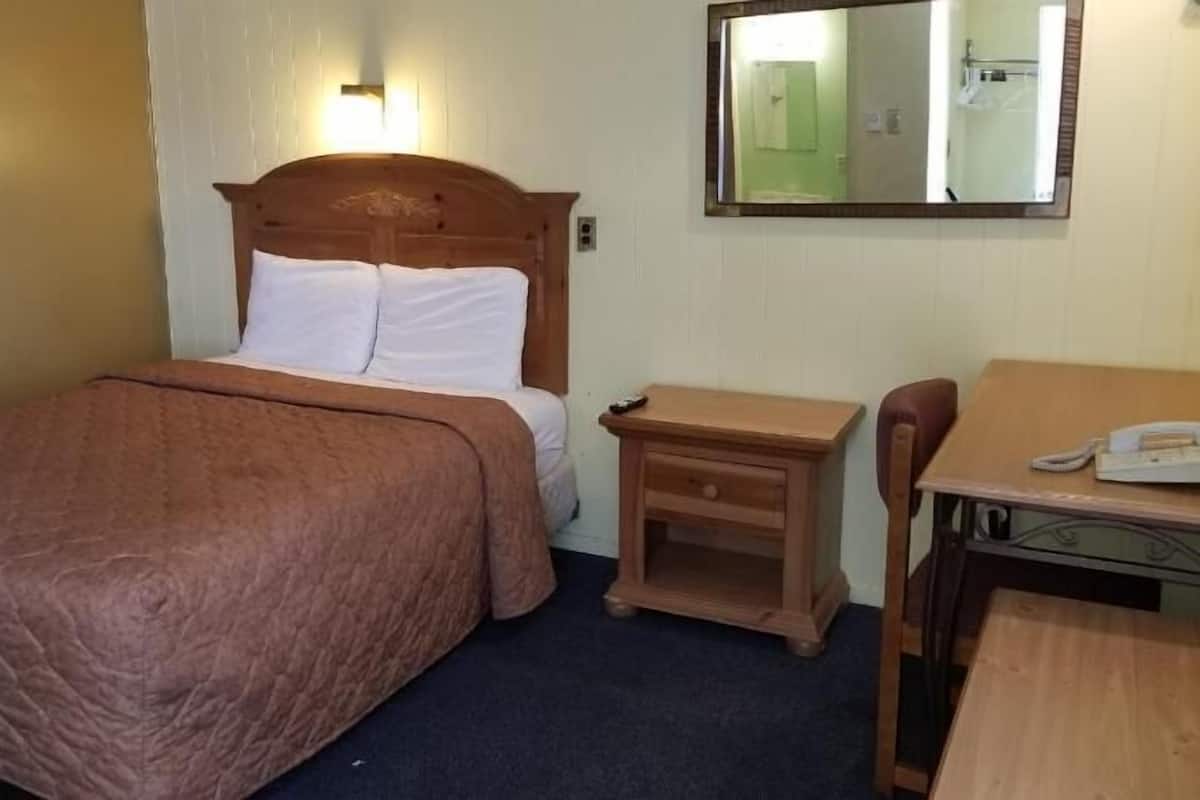 A hotel room with a single bed, a small bedside table, a chair, and a desk with a telephone.