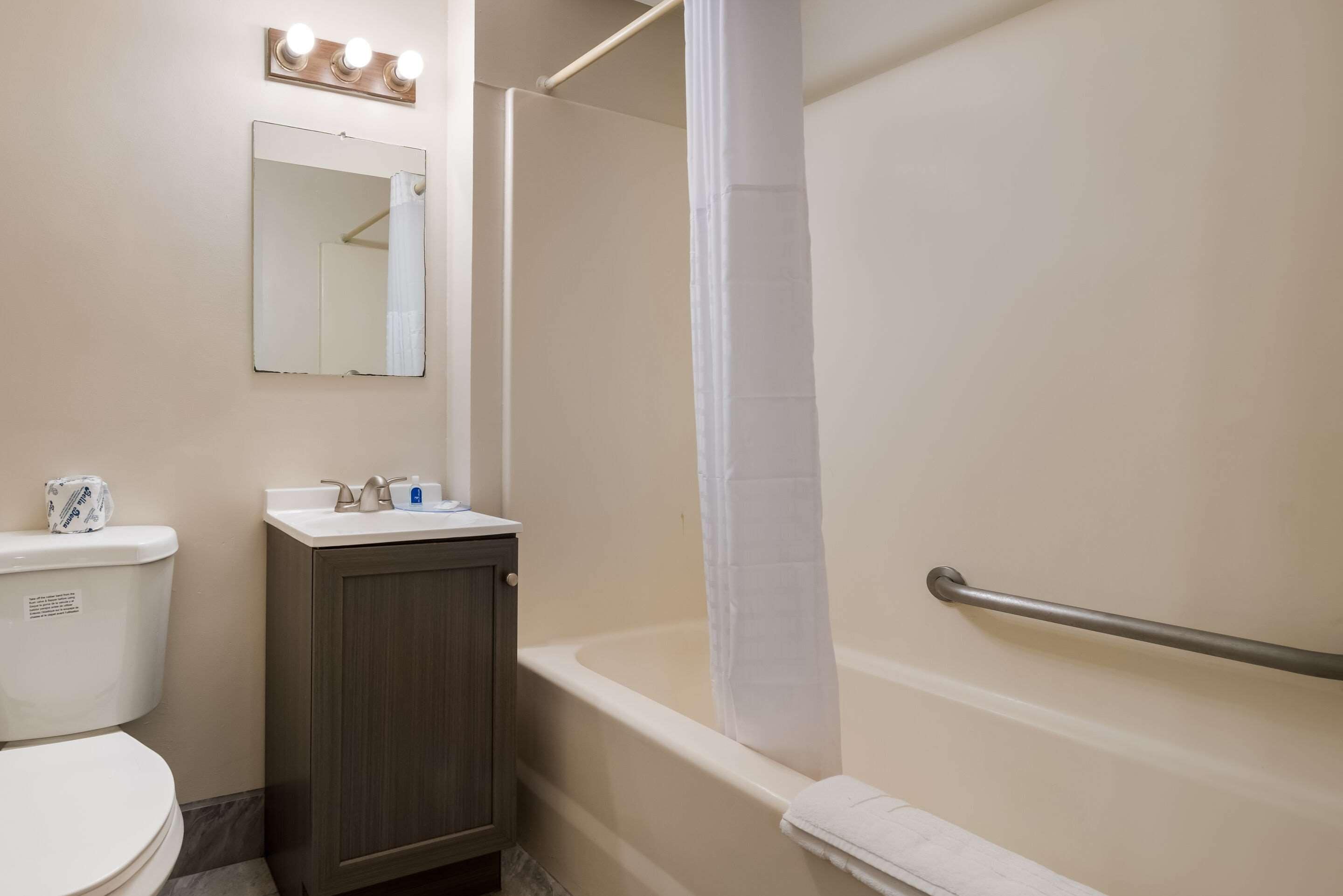 Un baño con inodoro, lavamanos, espejo y bañera con cortina de ducha.