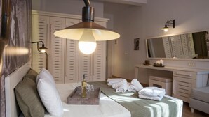A hotel room with a bed, a bedside table with a tray of items, a large mirror, and a wardrobe with louvered doors. - Elia Daliani (Chania)