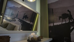 A room with a bed, a mirror, a wall-mounted picture, and a bedside table with candles and decorative items. - Elia Daliani (Chania)