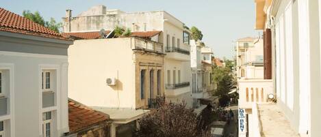 Una calle estrecha flanqueada por edificios, un sendero arbolado y una furgoneta estacionada.