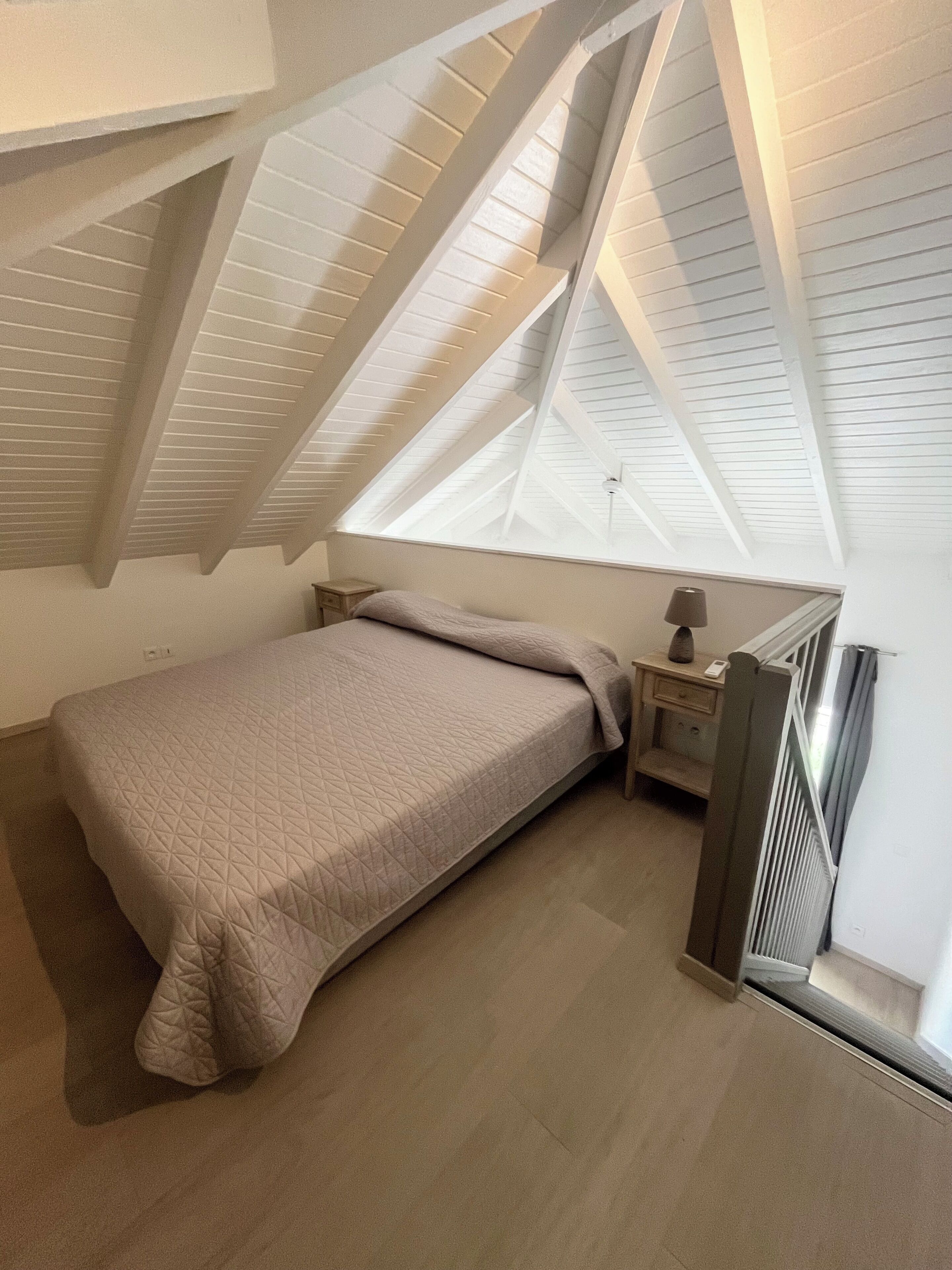 A bedroom with a sloped ceiling, a bed, a nightstand, a lamp, and a radiator.