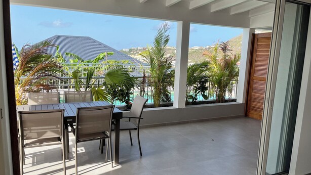 A balcony with a table and chairs, overlooking a swimming pool and greenery. - Colombus Résidence (Oyster Pond)