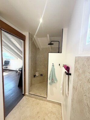 Un baño moderno con cabina de ducha de vidrio, un perchero con una toalla rosa y un cabezal de ducha visible.