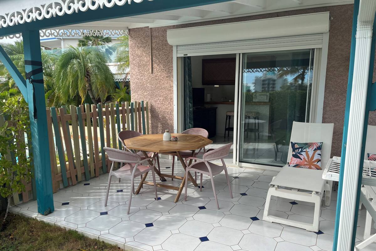 A patio with a wooden table and chairs, a glass door leading to a balcony, and a white railing.