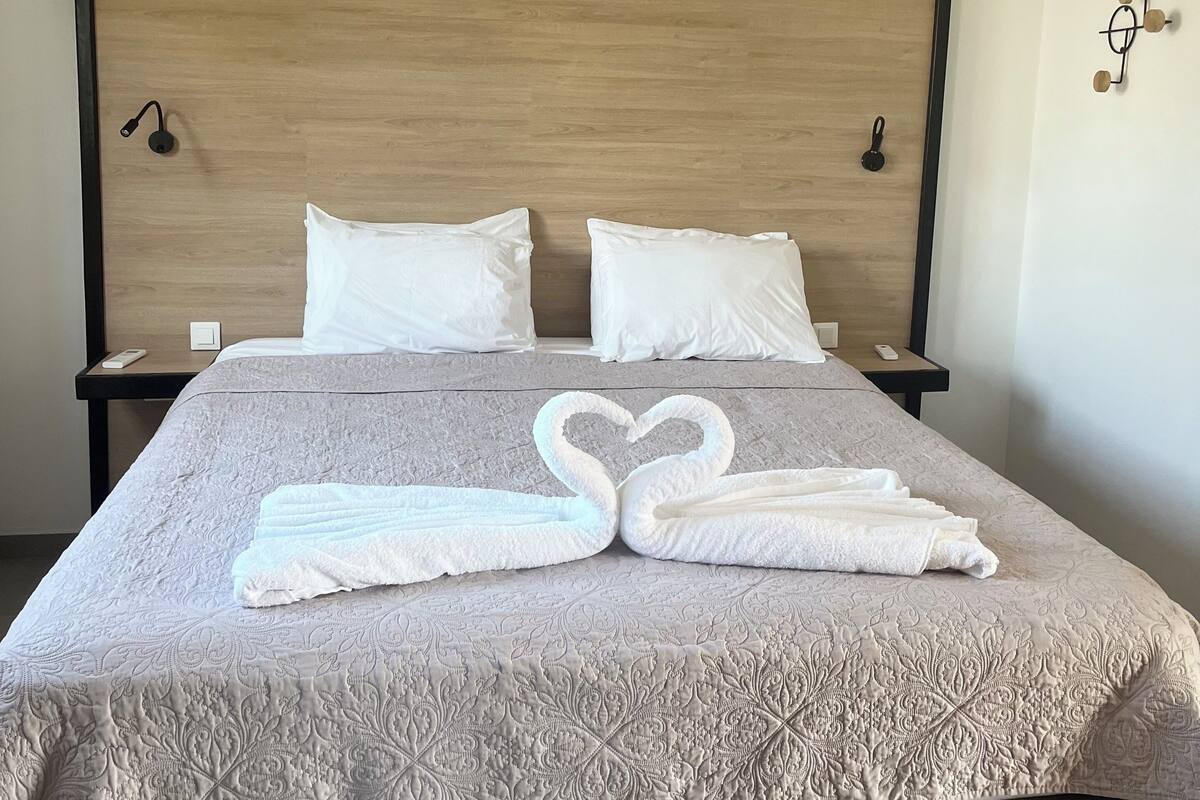 A neatly made bed with a patterned bedspread, two pillows, and a heart-shaped towel arrangement.