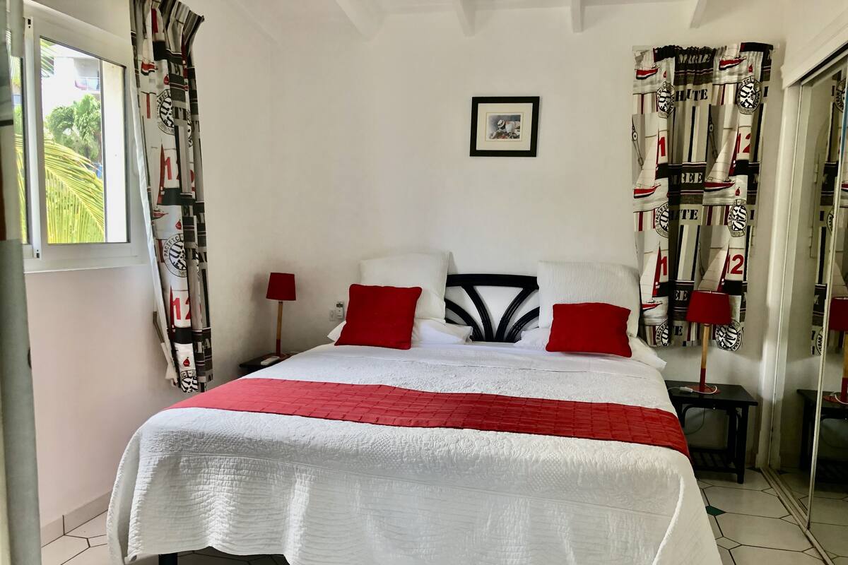 A neatly made bed with white and red bedding, a framed picture on the wall, and curtains with a sports team logo.