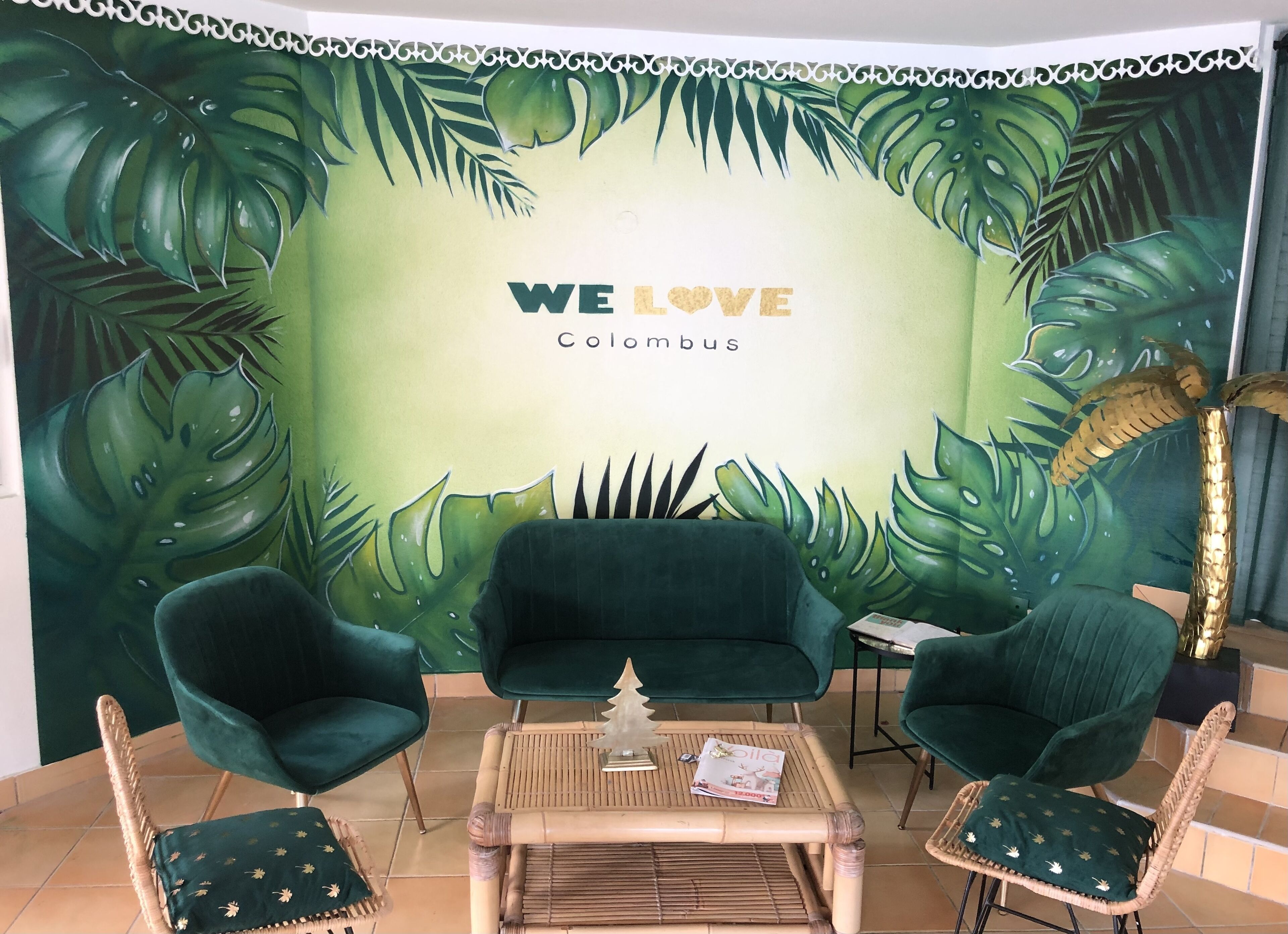 Una habitación con un mural de temática tropical, dos sillones verdes, una mesita y una planta decorativa.