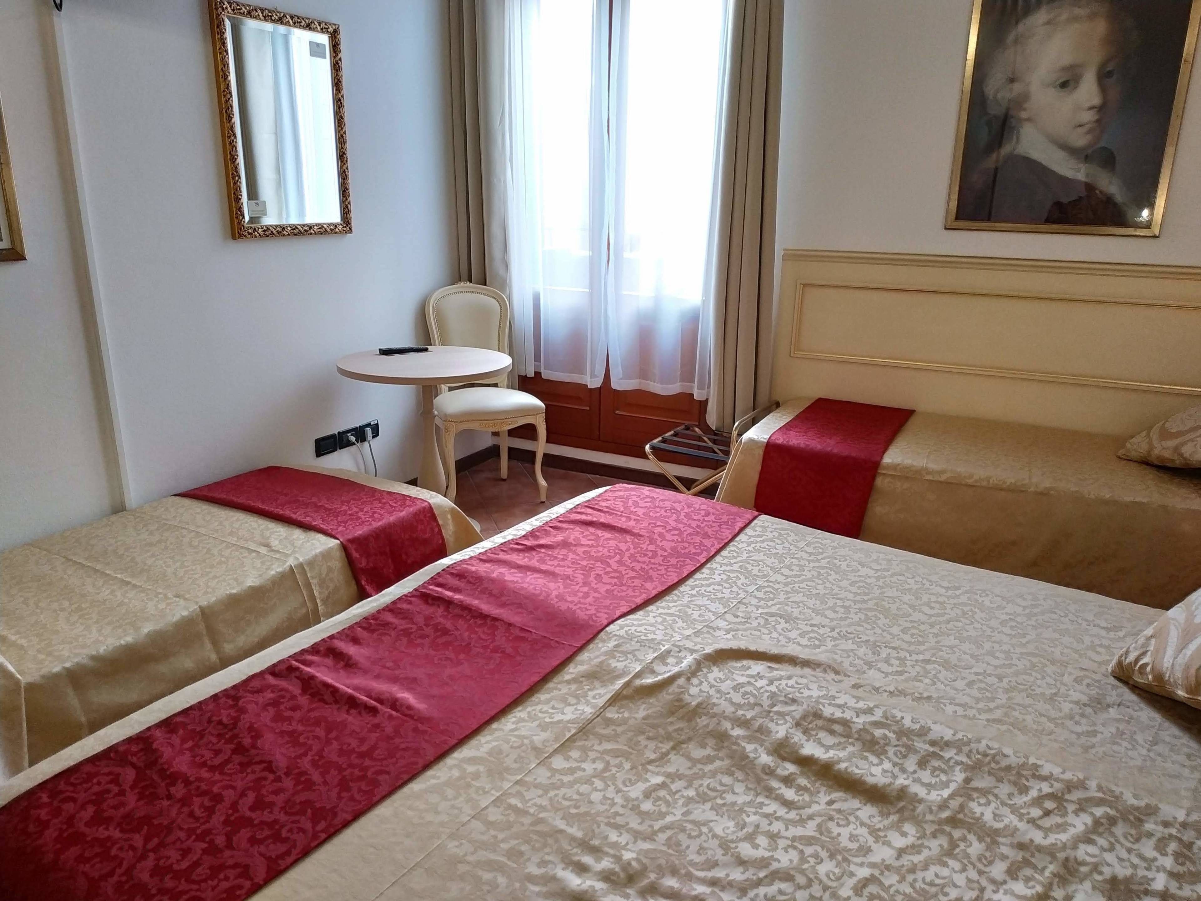 A hotel room with two single beds, a small table, a chair, and a window with curtains.