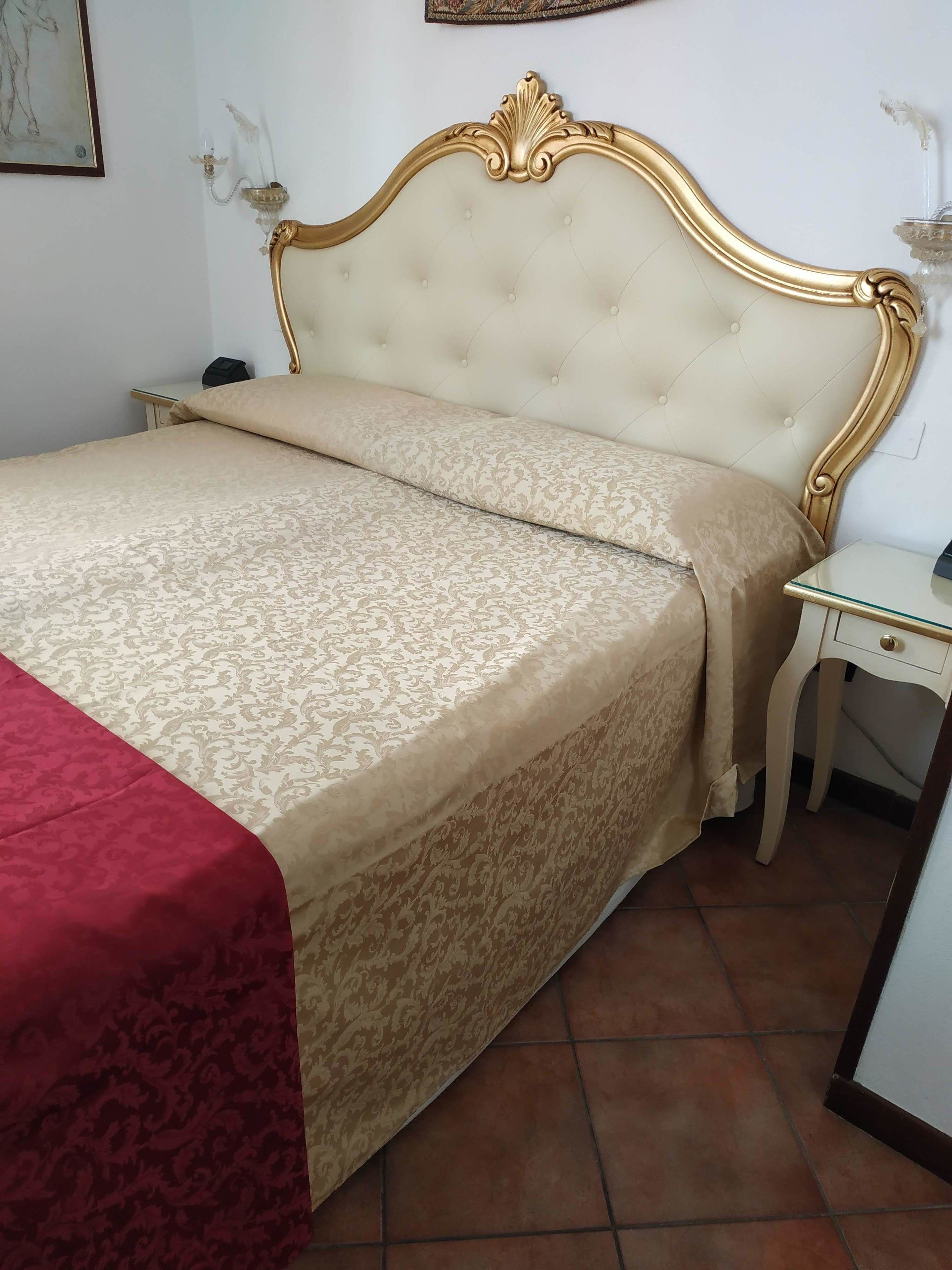 Ein Bett mit einer gebügelten Kopfteil, ein Nachttisch und eine rote Tagesdecke.