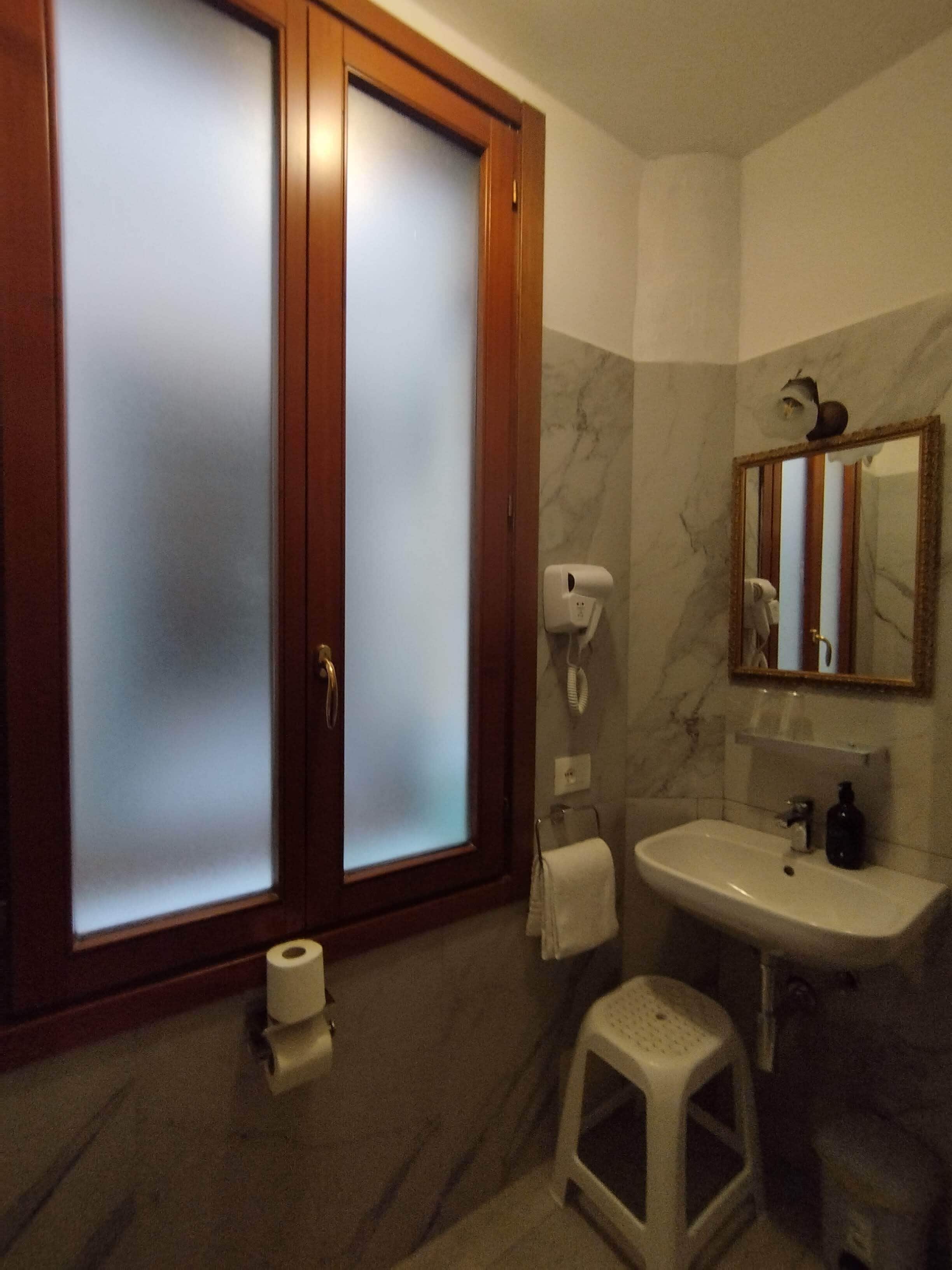 A bathroom with a wooden door, a white sink, a mirror, a towel rack, and a toilet paper roll.