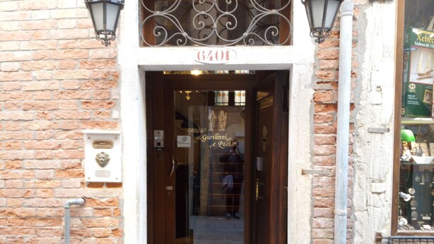 Un edificio de ladrillo con puerta de madera, un cartel sobre la puerta y un acceso con baldosas.