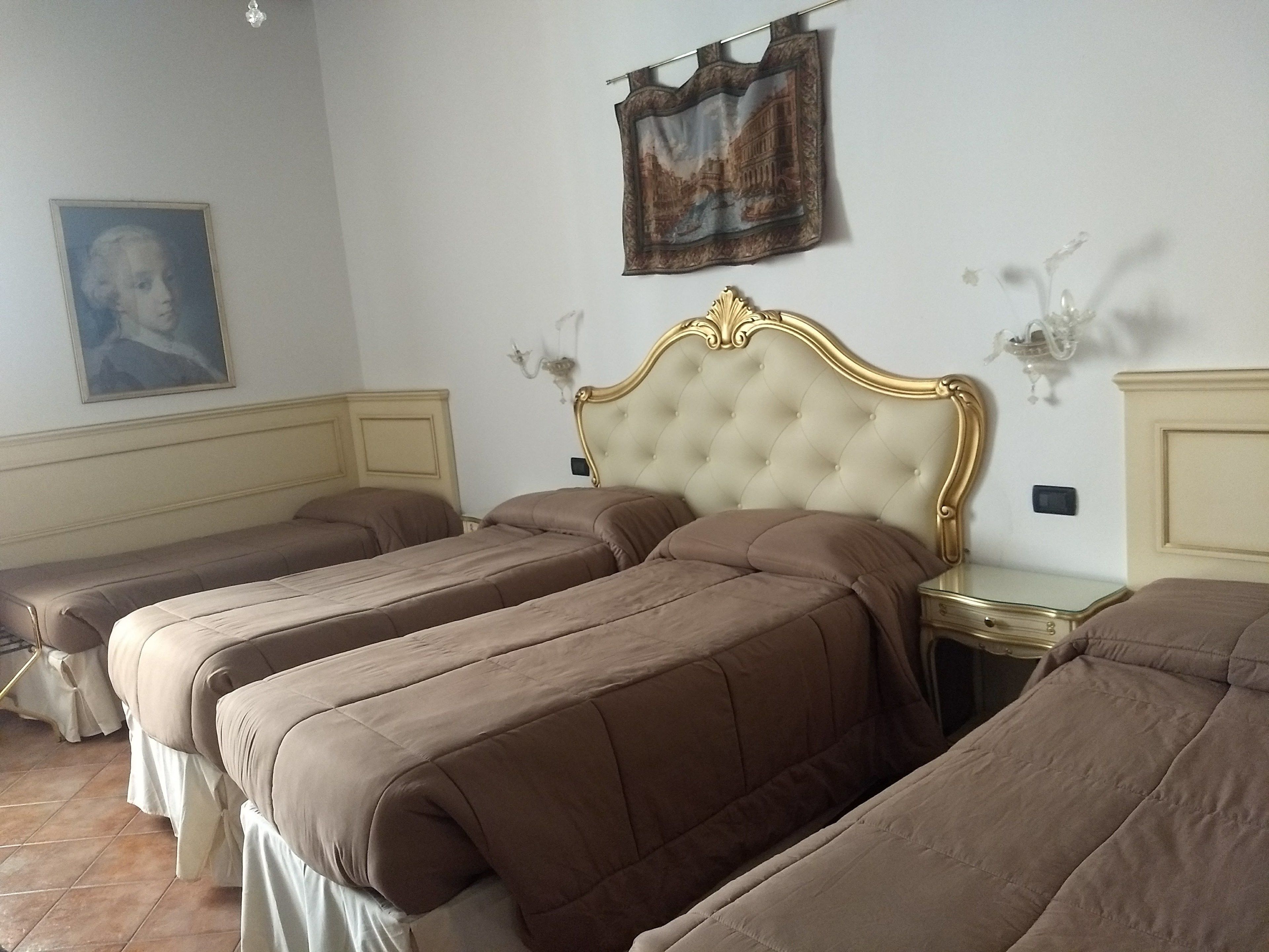 A hotel room with three single beds, a large painting on the wall, and a chandelier.