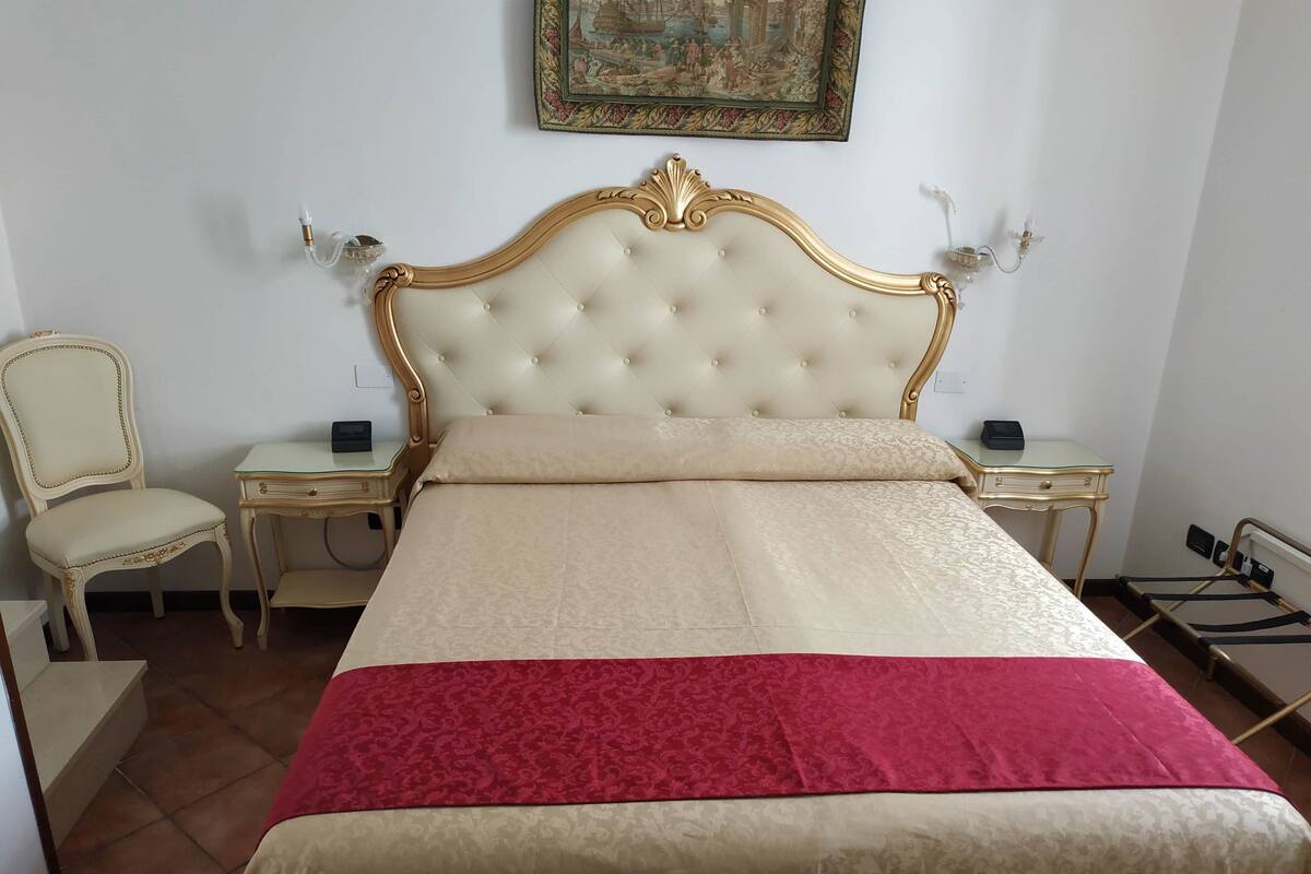 A hotel room with a large bed, two bedside tables, a chair, and a painting on the wall.
