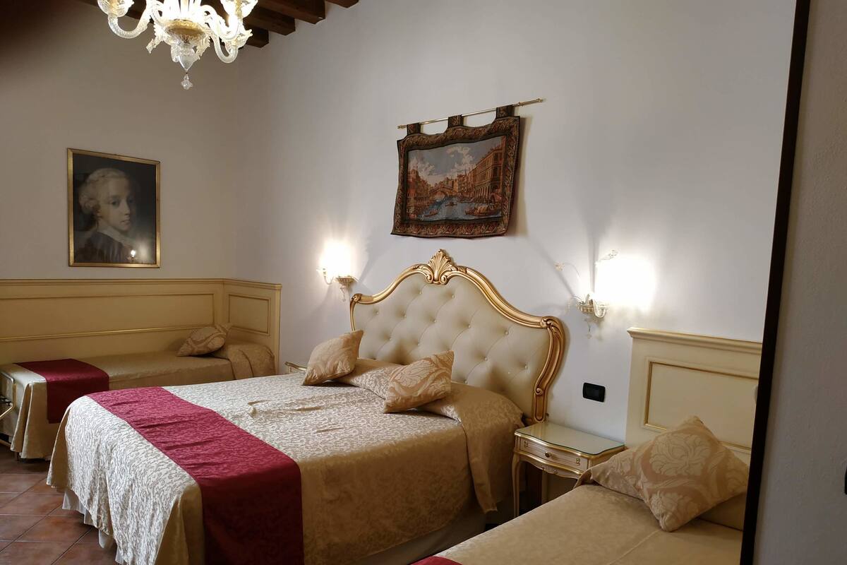 A hotel room with a large bed, two bedside tables, a chandelier, and a painting on the wall.