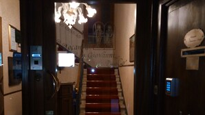 Una escalera conduce a un rellano con un candelabro, una placa con nombre y una puerta con una placa.