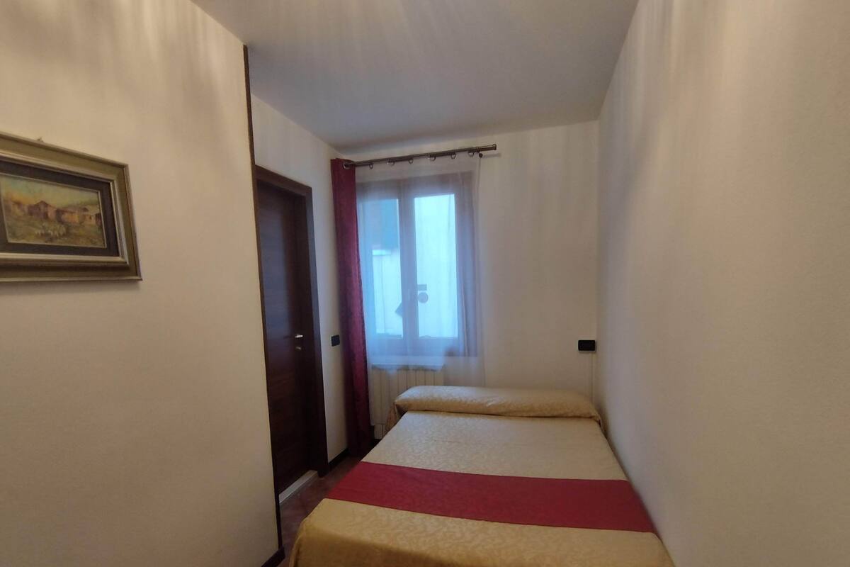 A narrow hotel room with a bed, a door, and a window with curtains.