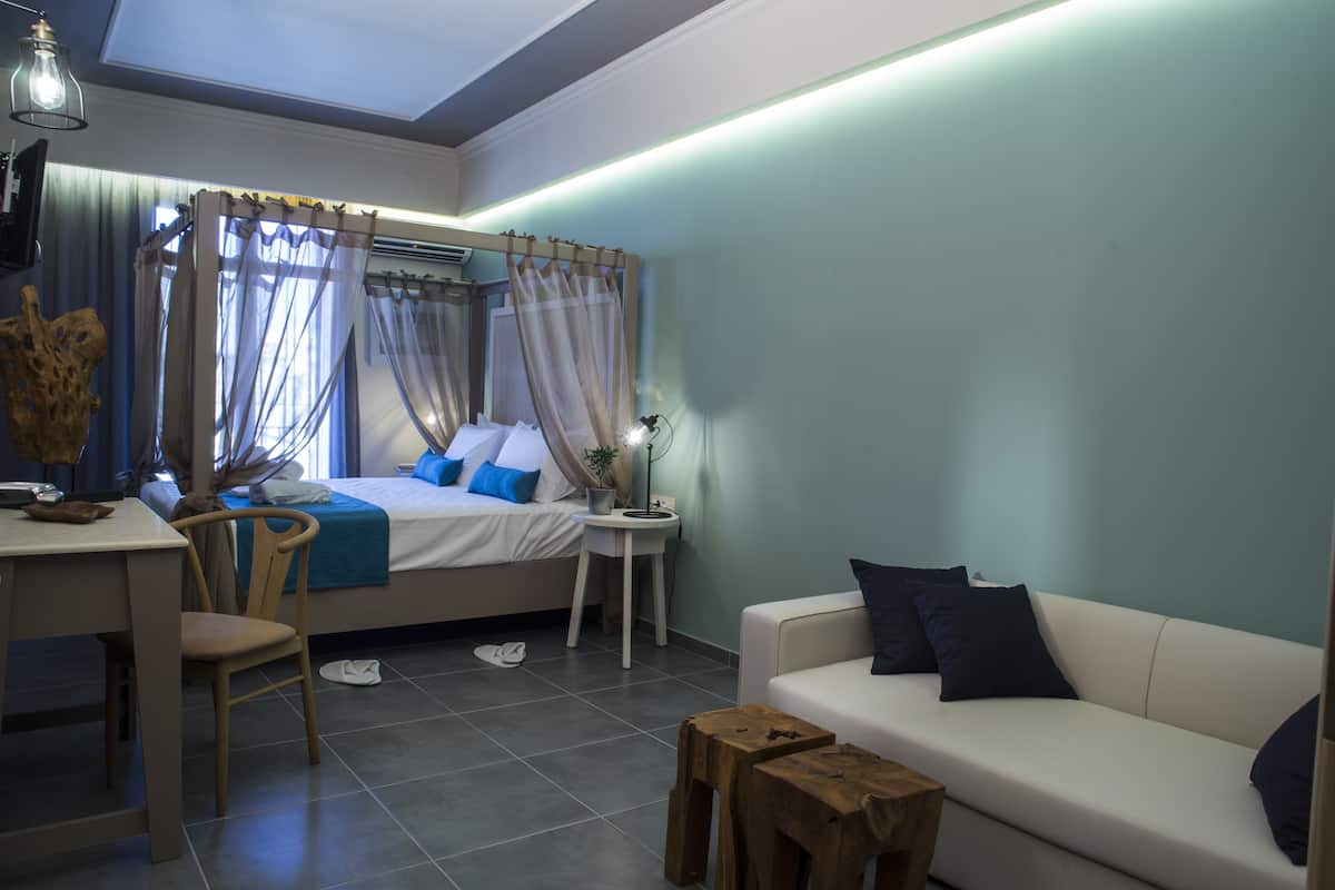 A modern bedroom with a bed, a desk, a chair, a sofa, and a small wooden stool.