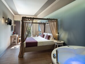 A bedroom with a four-poster bed, a sitting area with a chair and table, a large window, and a bathtub with a control panel. - Elia Potie (Chania)