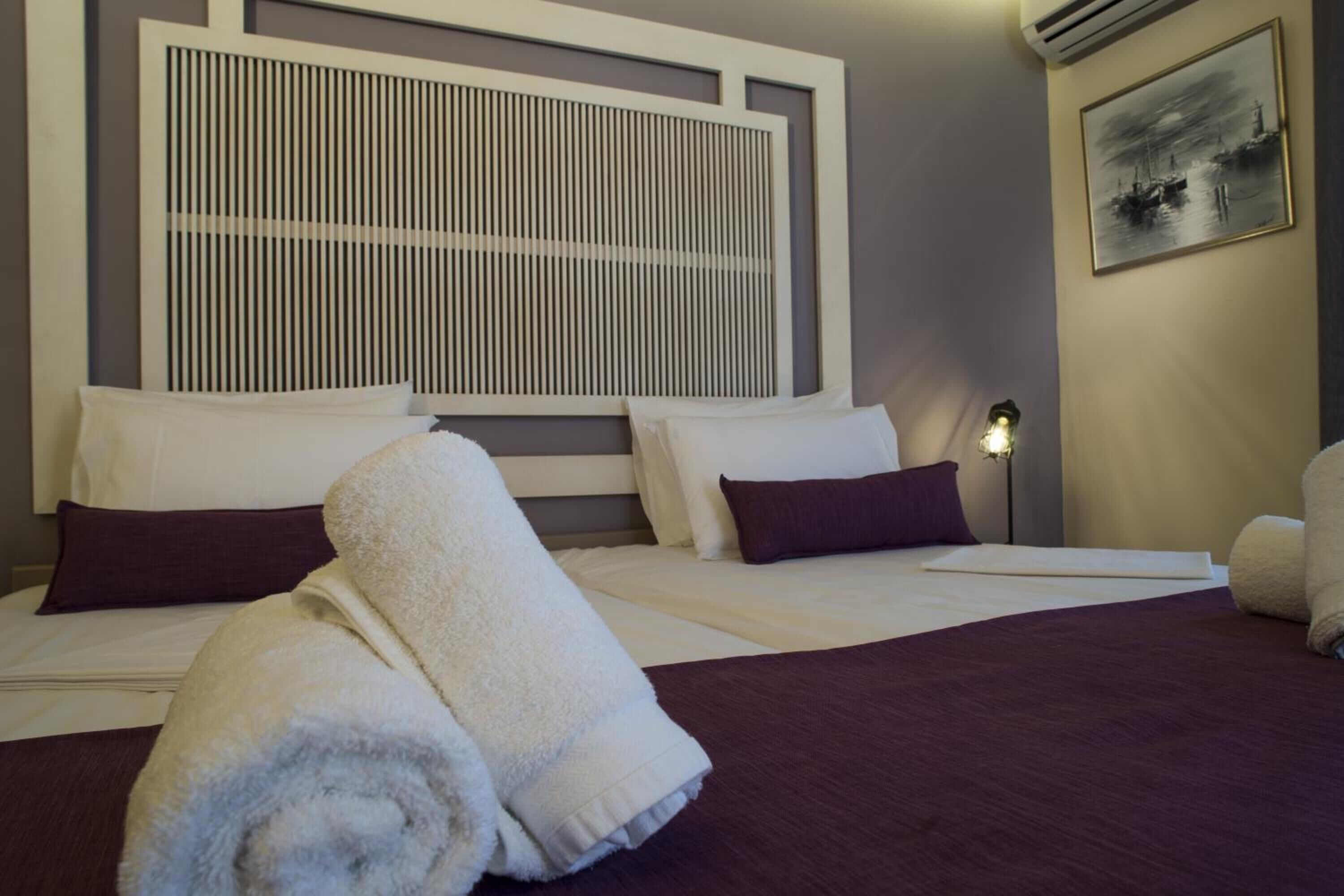 A hotel room with a large bed, a headboard with vertical slats, a nightstand with a lamp, and a framed picture on the wall.