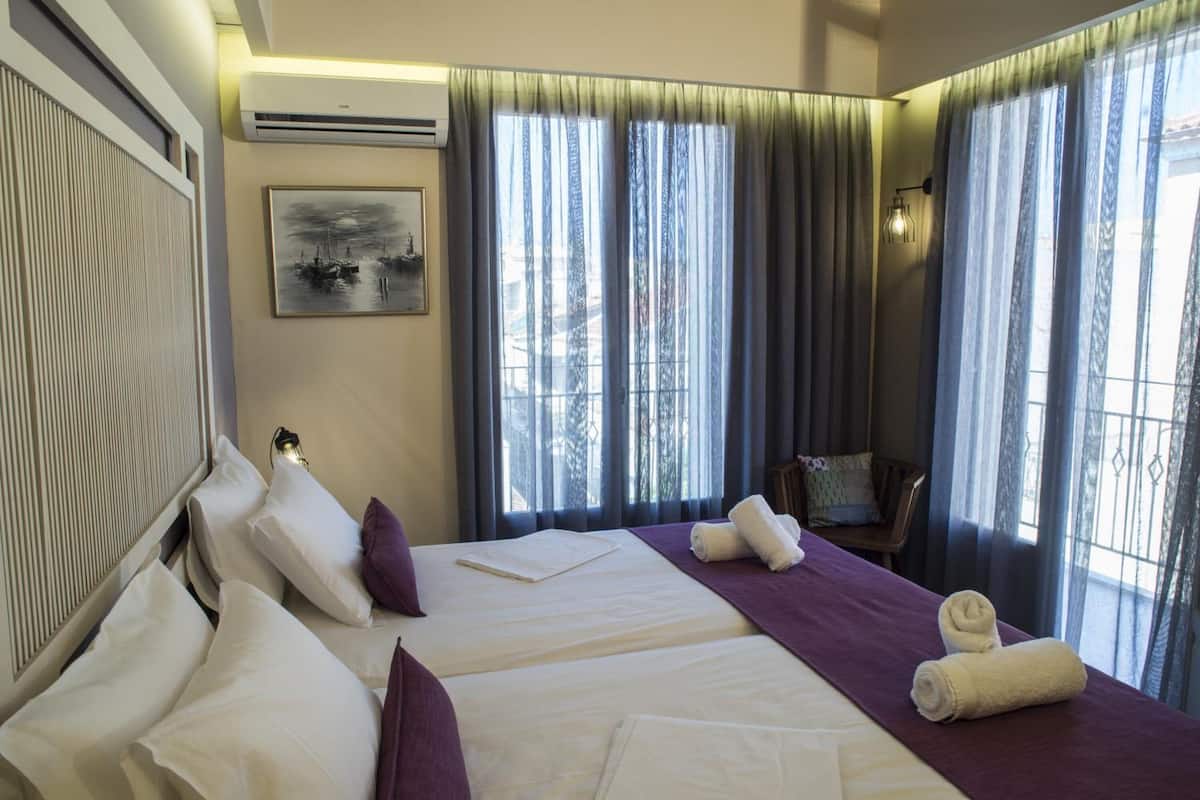 A hotel room with two beds, a large window with curtains, a painting on the wall, and a chair by the window.