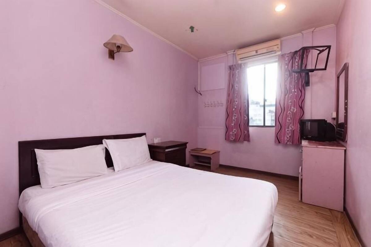 A bedroom with a bed, a nightstand, a desk, a mirror, and a window with curtains.