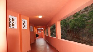 A corridor with orange walls, tiled floor, and windows overlooking a rocky landscape. - Rival Hotel (Cap-Haitien)
