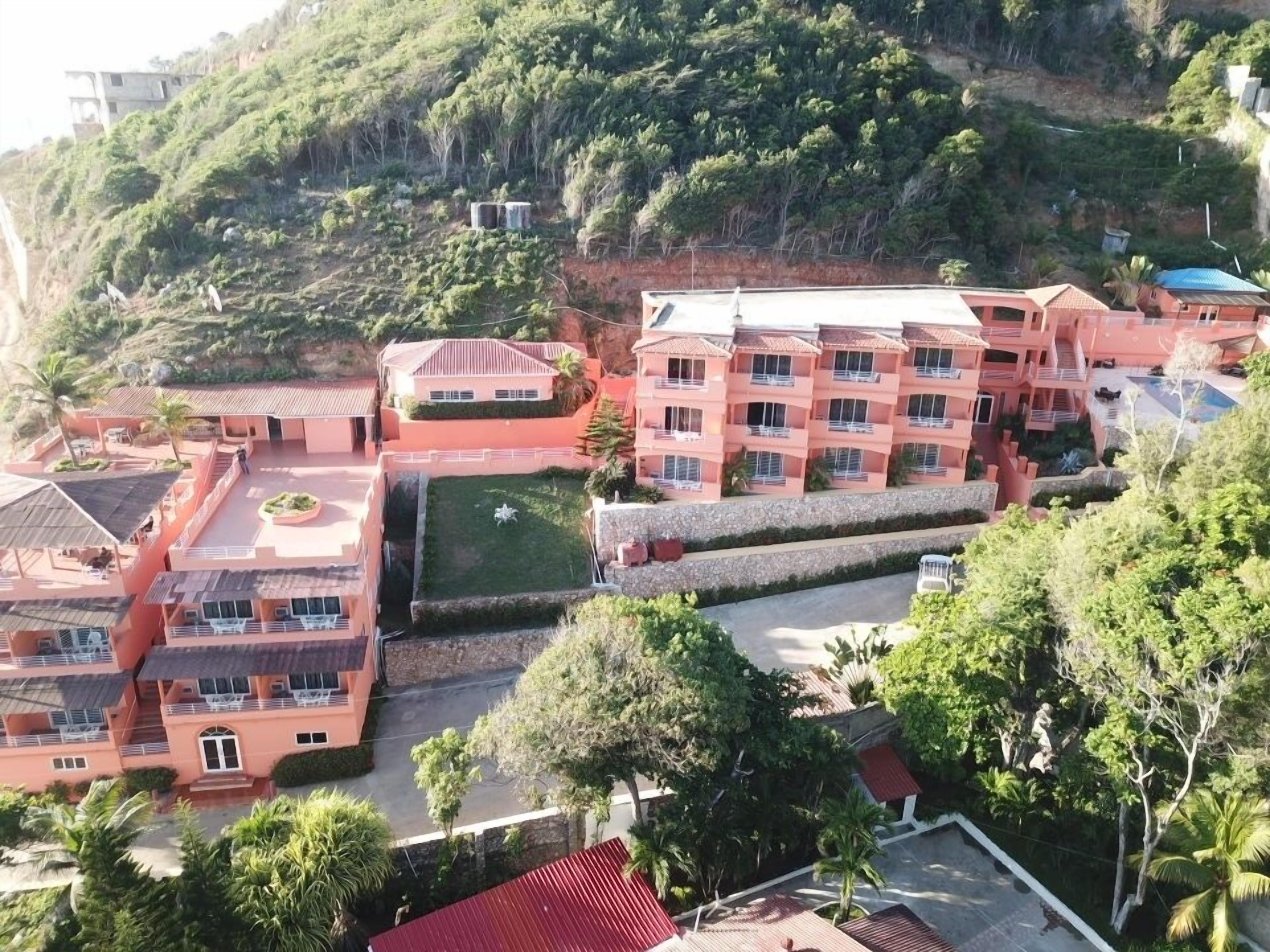 A multi-story hotel with balconies, a swimming pool, and lush greenery surrounding the property.