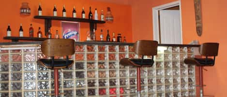 Zona de bar con un panel de vidrio, taburetes de madera y estantes con botellas.