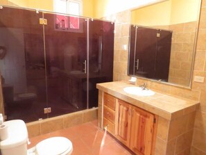 A bathroom with a glass-enclosed shower, a sink with a mirror above it, and wooden cabinets.