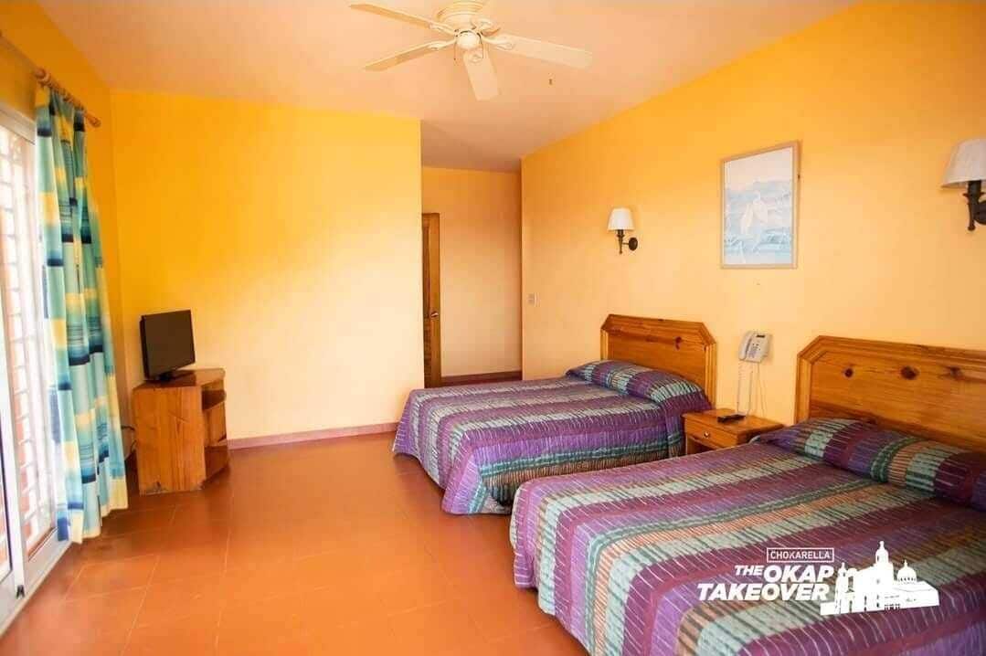 Een kamer met twee bedden, een plafondventilator, een televisie en een deur.