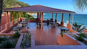 A covered outdoor seating area with tables and chairs, overlooking the ocean. - Rival Hotel (Cap-Haitien)