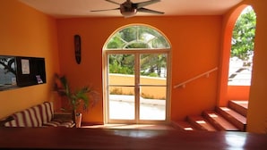 A room with a large window, a ceiling fan, a staircase, and a striped sofa. - Rival Hotel (Cap-Haitien)