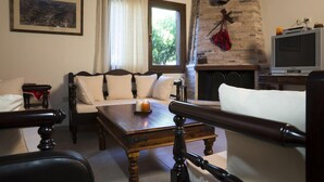 A cozy living room with a stone fireplace, a sofa, a wooden coffee table, and a television. - Elia Therissos Maisonettes (Chania)
