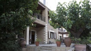 A stone building with a balcony, potted plants, and a staircase leading to the entrance. - Elia Therissos Maisonettes (Chania)