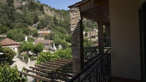 A balcony with stone pillars, a wooden railing, and a view of a hillside with houses. - Elia Therissos Maisonettes (Chania)