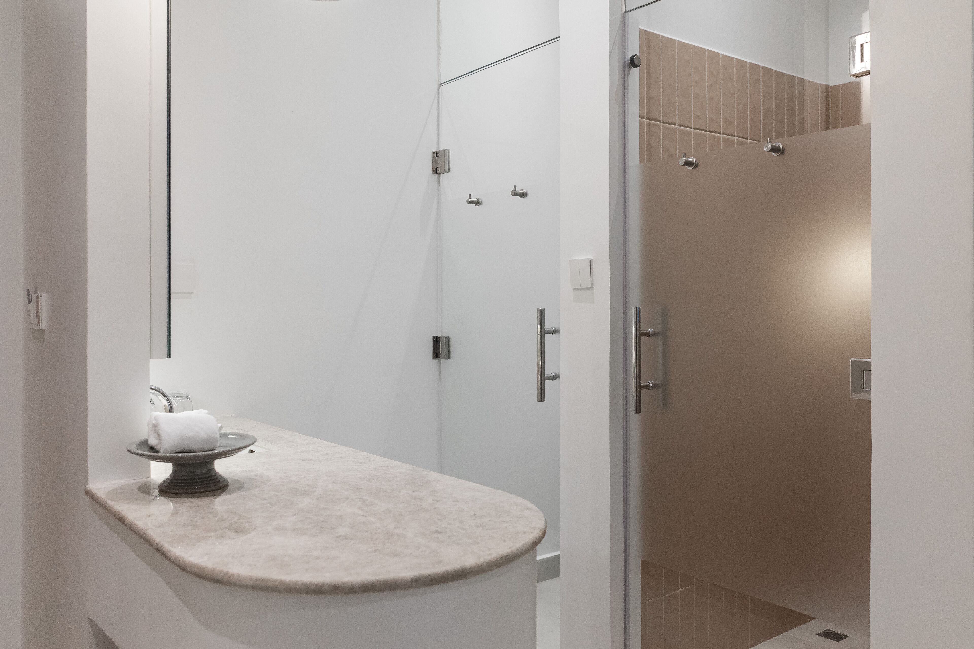 Een moderne badkamer met een gebogen wastafelblad, een douchecabine met glazen wanden en een witte handdoek op een decoratieve schaal.