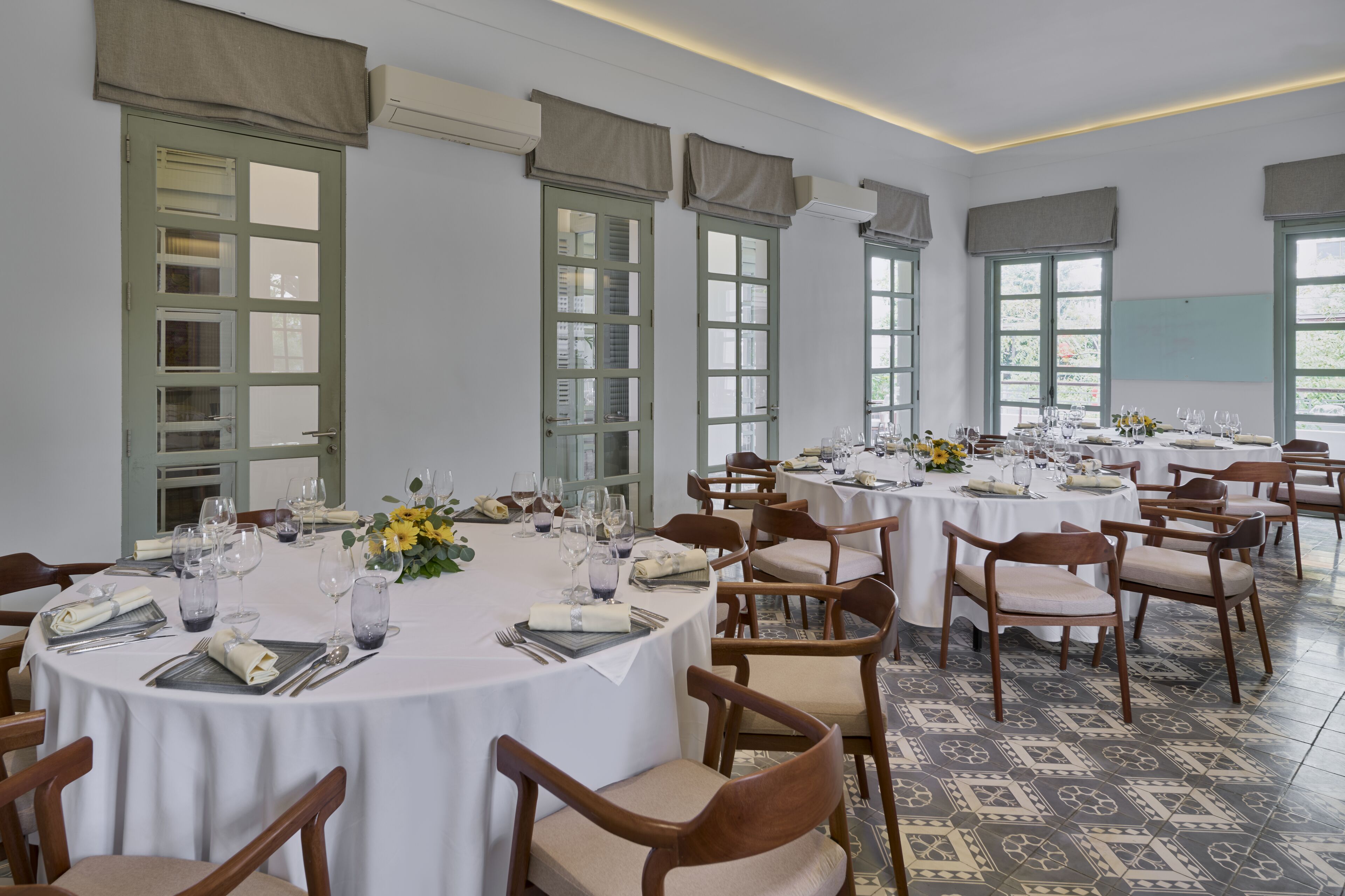 A dining area with multiple round tables set for a meal, each with chairs, plates, cutlery, and glasses.