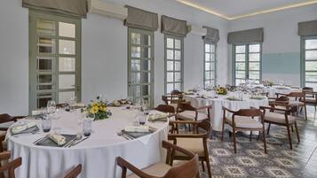 A dining area with multiple round tables set for a meal, each with chairs, plates, cutlery, and glasses.