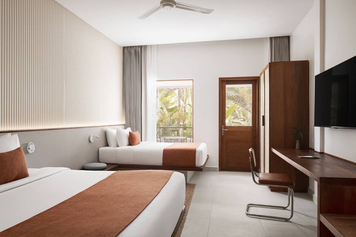 Ein Hotelzimmer mit Bett, Schreibtisch, Stuhl, Fernseher und einem Balkon mit Blick auf Grünflächen.