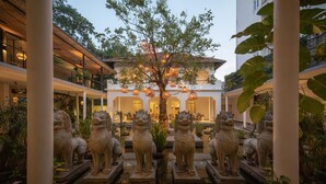 A courtyard with a central tree, surrounded by stone lion statues, and a building with a tiled roof in the background. - Plantation Urban Resort & Spa (Phnom Penh)
