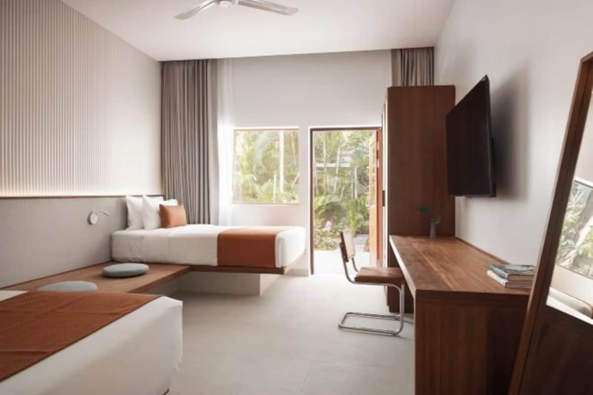 A modern hotel room with a bed, a desk, a chair, and a TV.