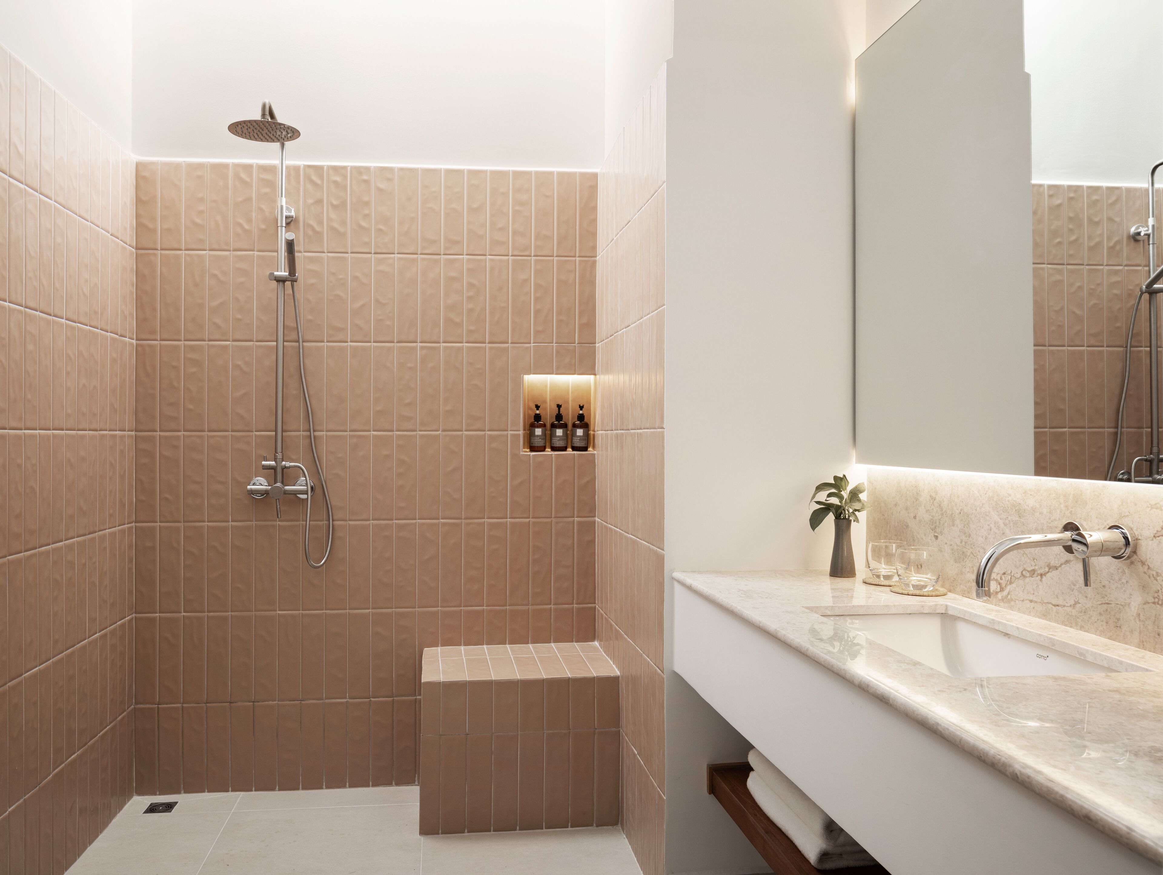Uma casa de banho moderna com cabine de duche, toucador com espelho e prateleira com artigos de higiene pessoal.