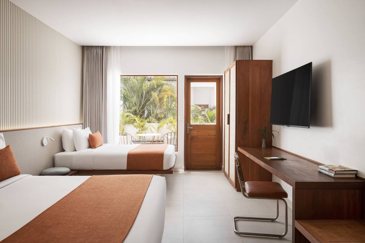 Ein Hotelzimmer mit zwei Betten, einem Schreibtisch, einem Fernseher und einem Balkon mit Blick ins Grüne.