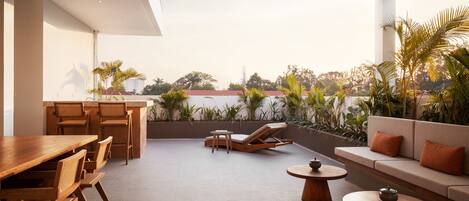 A spacious patio with a wooden dining table, chairs, a sofa, and lounge chairs. There are potted plants and a view of the cityscape.