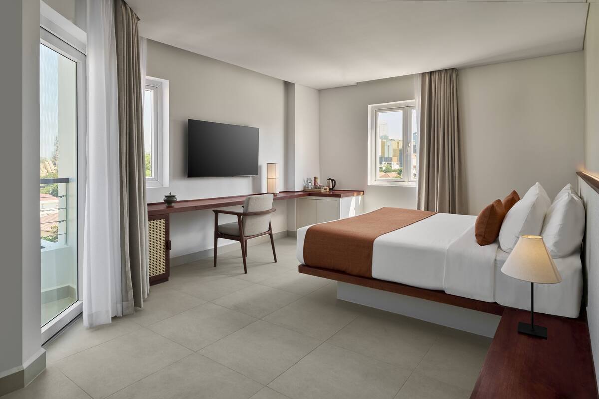 Ein Hotelzimmer mit Bett, Schreibtisch, Sessel, Fernseher und großen Fenstern.