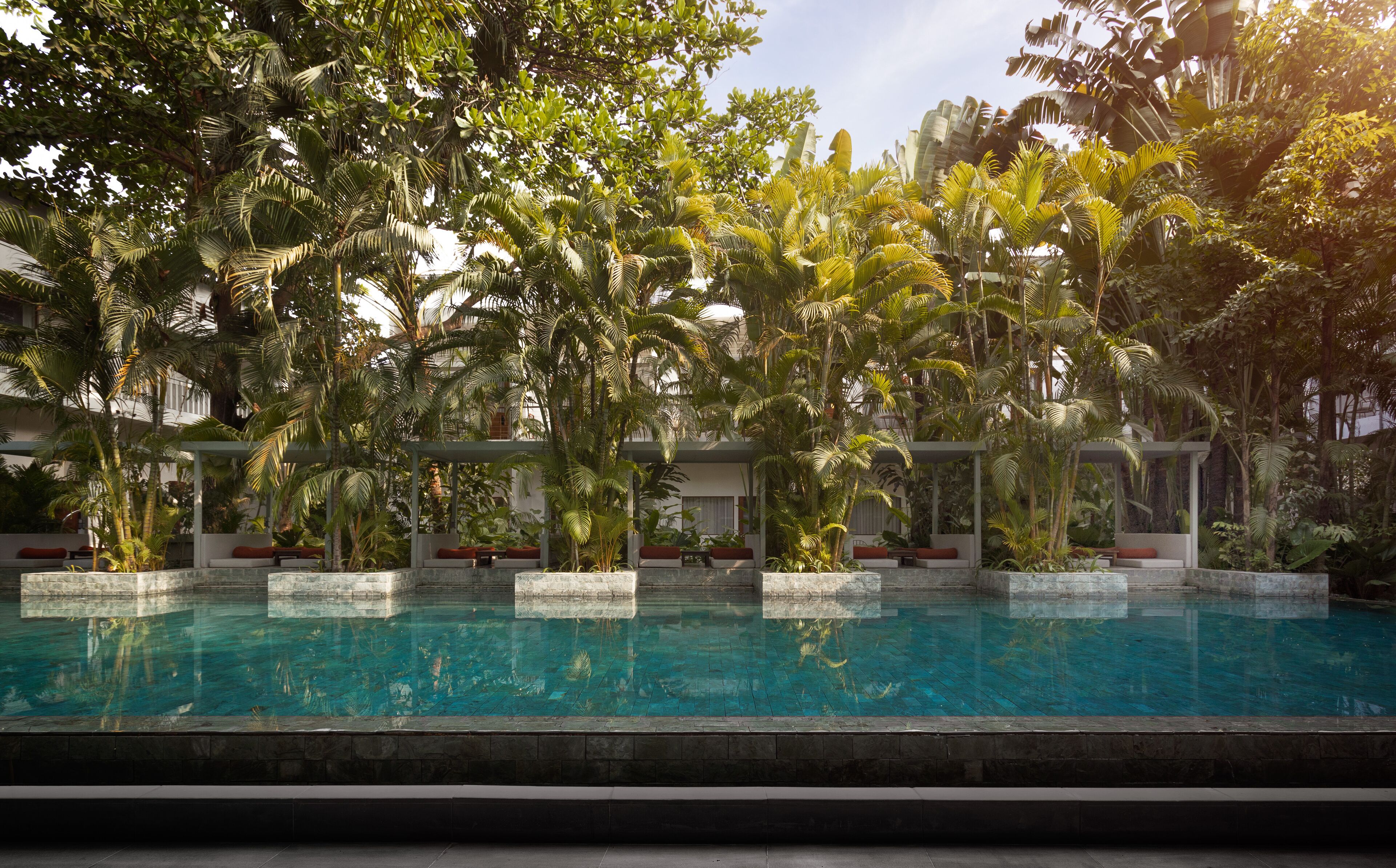 A swimming pool surrounded by lush tropical plants and a building with a covered seating area.