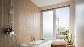 A modern bathroom with a freestanding bathtub, a showerhead, and a window with a view of a balcony.