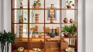 A modern living room with a wooden shelving unit displaying various decorative items and plants. - Plantation Urban Resort & Spa (Phnom Penh)