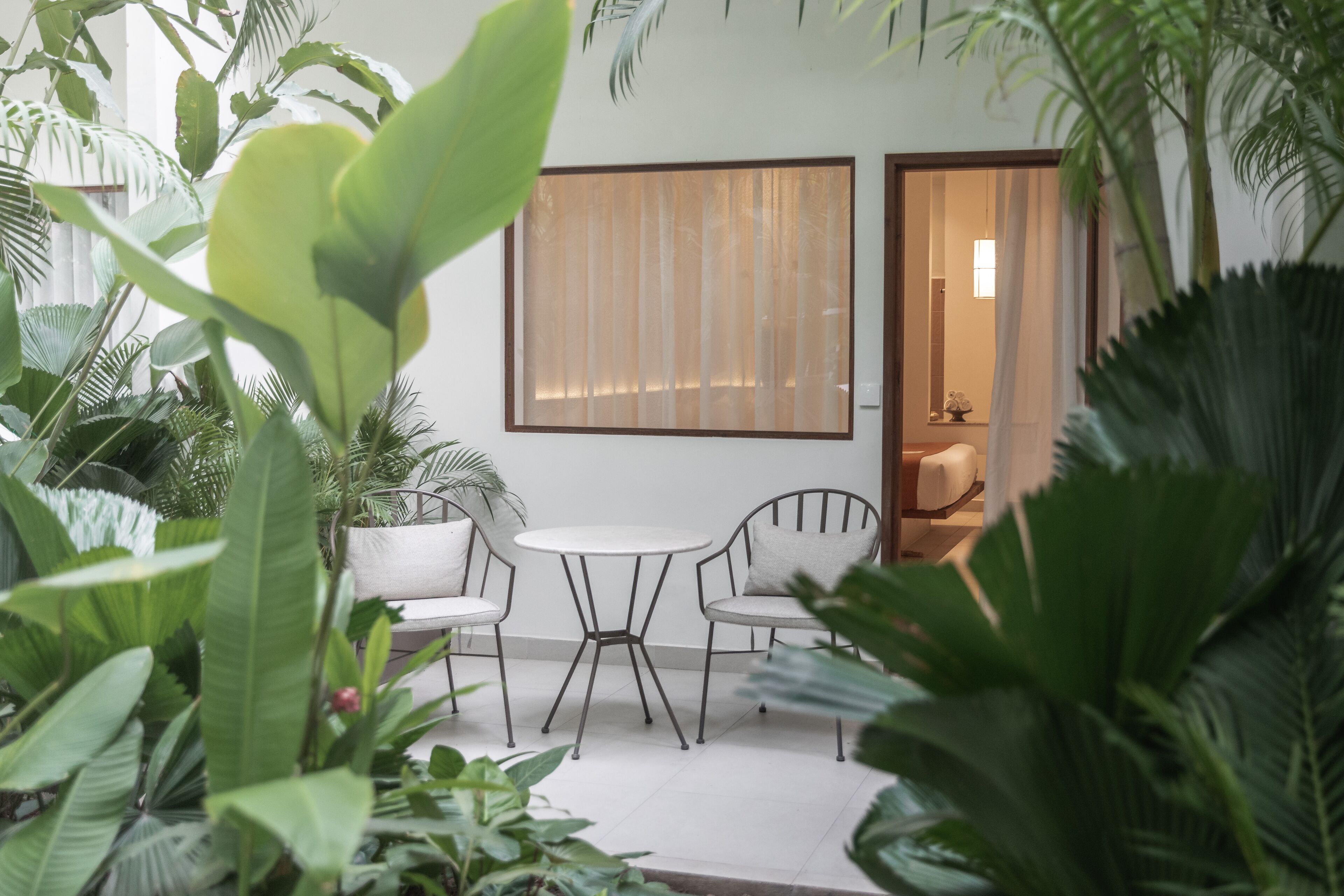 Un espace patio avec une table blanche et deux chaises, entouré d’une végétation luxuriante.